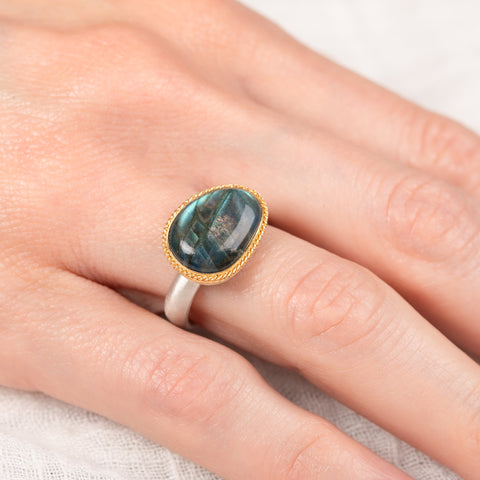 Ring with a labradorite gemstone on a finger against a white background