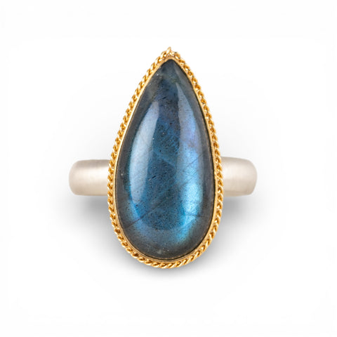 Ring with a teardrop-shaped labradorite gemstone and gold bezel with silver band on a white background