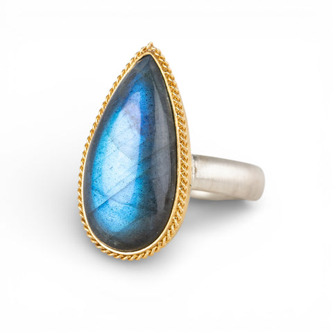 Ring with a teardrop-shaped labradorite gemstone and gold bezel with silver band on a white background