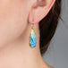 Teardrop-shaped earring with a labradorite gemstone worn by a person.