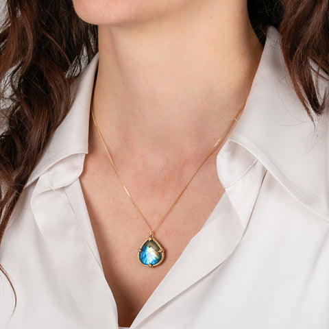 Necklace with a blue labradorite gemstone pendant worn by a person in a white shirt