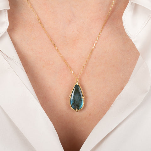 Gold necklace with a labradorite teardrop pendant on a person wearing a white shirt