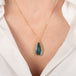 Gold necklace with a labradorite teardrop pendant on a person wearing a white shirt