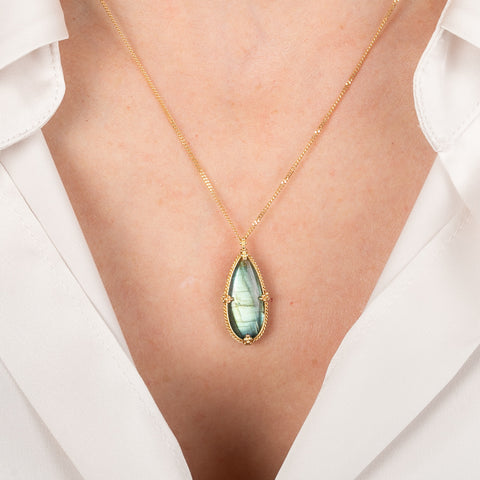 Gold necklace with a labradorite on a person wearing a white shirt