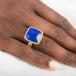 Gold and silver ring with a lapis stone on a person's finger against a white background
