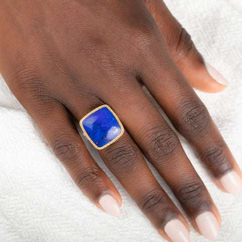 Gold and silver ring with a lapis stone on a person's finger against a white background