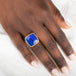 Gold and silver ring with a lapis stone on a person's finger against a white background