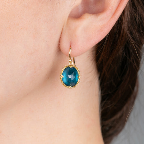 Gold earrings with london blue topaz gemstones worn on a person