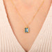 A gold necklace featuring a london blue topaz stone set in an 18k gold bezel, worn on a person's neck.