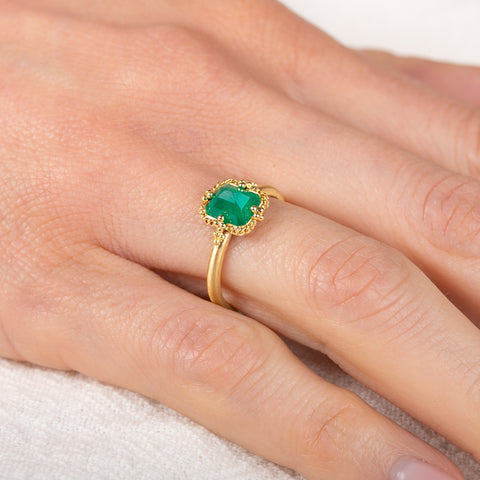 Gold ring with an emerald gemstone on a person's finger against a neutral background