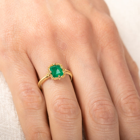 Gold ring with an emerald gemstone on a person's finger