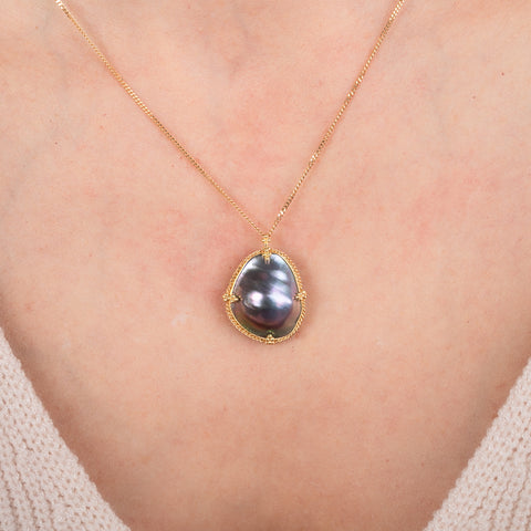 Gold necklace with a mabe pearl pendant on a person's neck