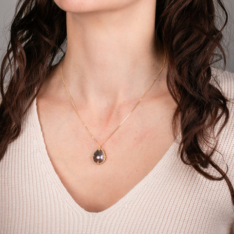 Gold necklace with a mabe pearl pendant on a person's neck