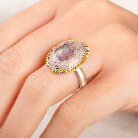 Close up of a person wearing a handmade fine jewelry ring with a Mexican Opal stone, gold bezel and sterling silver band 