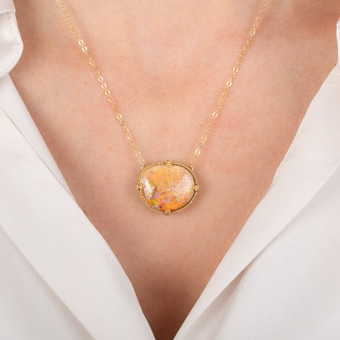 Gold necklace with a large Mexican opal stone on a person