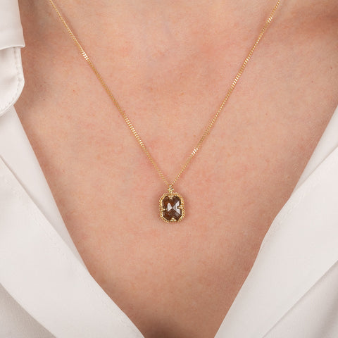 Gold necklace with a brown diamond pendant on a person wearing a white shirt