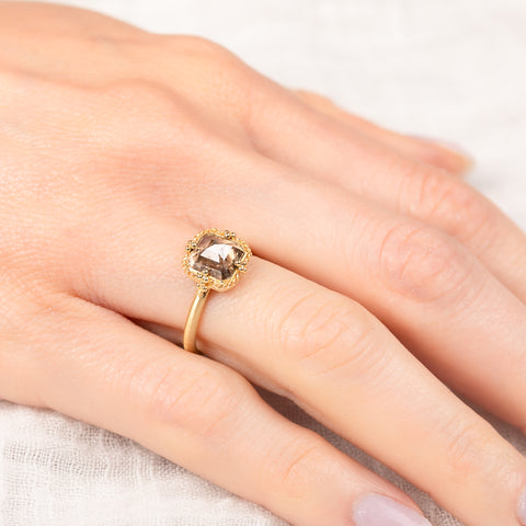Gold ring with a diamond gemstone on a hand against a neutral background