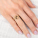 Gold ring with a diamond on a hand with light pink nail polish against a white fabric background