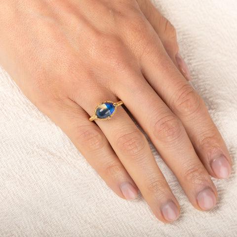 Gold ring with a moonstone on a hand against a white background