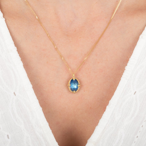 Gold necklace with a moonstone pendant on a person wearing a white garment.