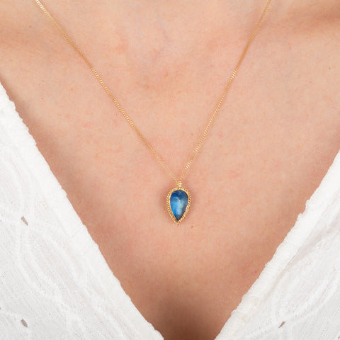 Gold necklace with a blue moonstone pendant on a person wearing a white top.