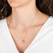 Gold necklace with a blue moonstone teardrop pendant worn by a person in a white top