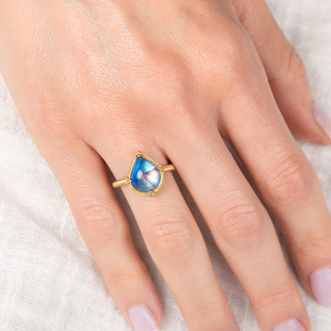 Gold ring with a blue teardrop-shaped moonstone held in hand