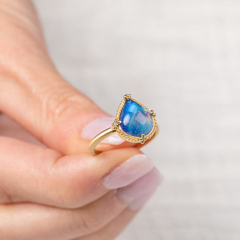 Gold ring with a blue teardrop-shaped moonstone held in hand