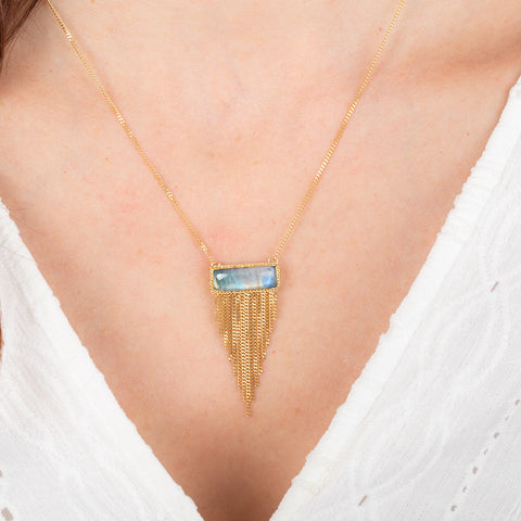 Gold necklace with a moonstone pendant on a person wearing a white top.