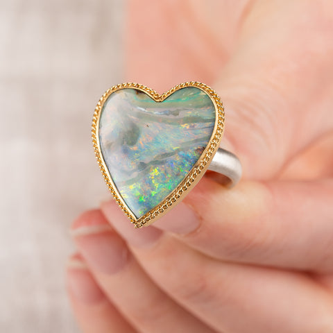 Hand holding a boulder opal heart ring with gold bezel and sterling silver band