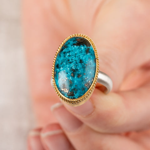 Close up of hand holding turquoise ring with gold bezel and sterling silver band