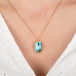 Gold necklace with a turquoise pendant worn by a person against a white background