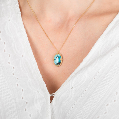 Gold necklace with a turquoise pendant worn by a person against a white background