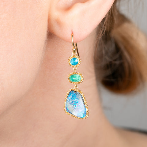 Gold earrings with apatite, emerald and boulder opal gemstones worn by a person