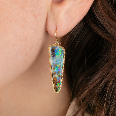Close-up of a woman wearing a colorful boulder opal earring with gold frame.