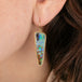 Close-up of a woman wearing a colorful boulder opal earring with gold frame.