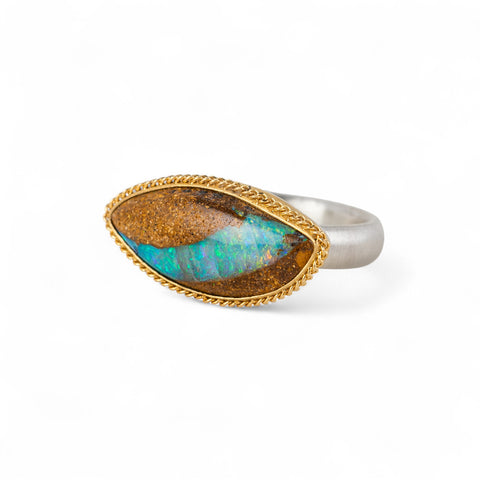 Ring with an opal stone, gold setting and silver band on a white background