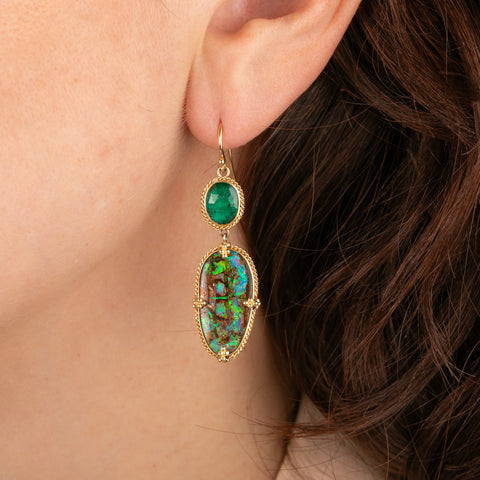 Pair of gold earrings with emerald and opalized wood stones worn by a person