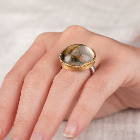 A handcrafted ring with rutilated quartz set in an 18k gold bezel, with a sterling silver band