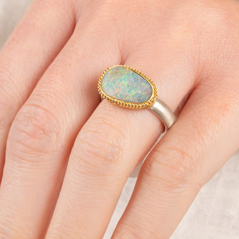 Close up of person wearing a handmade fine jewelry boulder opal ring with an 18k gold bezel and sterling silver band