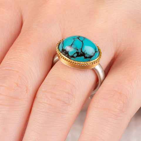 Close up of hand wearing a turquoise ring with gold bezel and sterling silver band