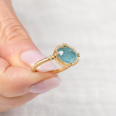 Gold ring with a blue aquamarine gemstone held by a hand on a light background