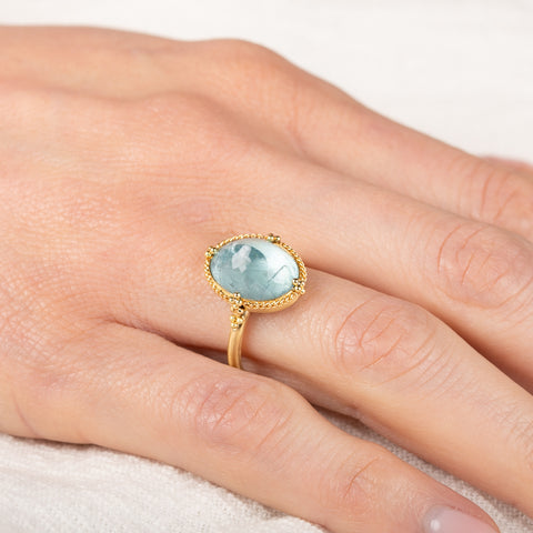 Gold ring with a blue aquamarine gemstone on a person's finger