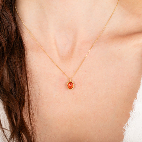 Gold necklace with a fire opal pendant on a person's neck
