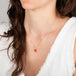 Close-up of a person wearing a delicate necklace with a fire opal pendant