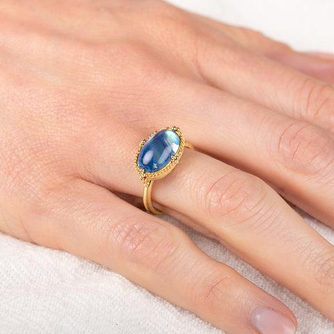 Gold ring with a moonstone on a person's finger against a white background