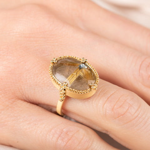 Gold ring with a rutilated quartz gemstone on a person's finger