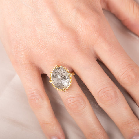 Gold ring with a tourmalated quartz stone on a hand