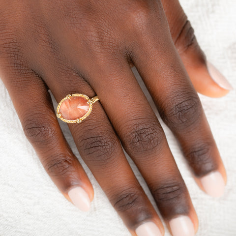 Gold ring with an Oregon sunstone on a person's finger against a neutral background