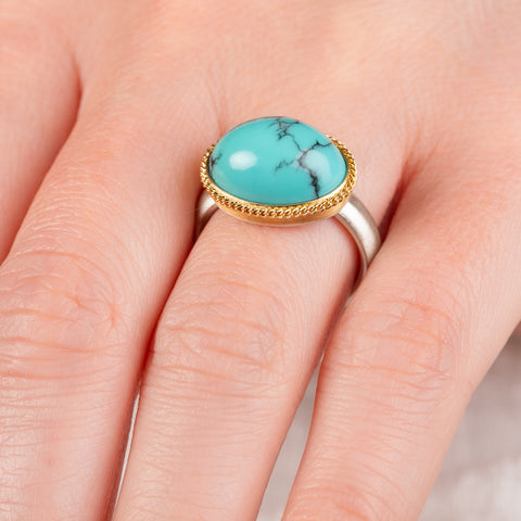 Close up of hand wearing a turquoise ring with gold bezel and sterling silver band on white background